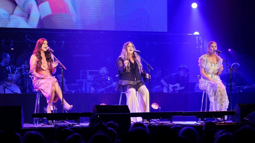 The McClymonts sitting on stools on stage and singing