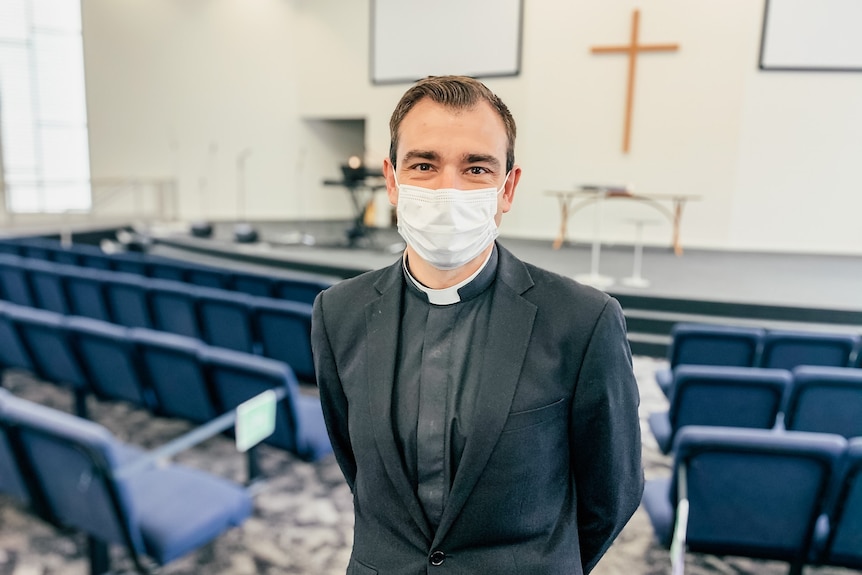 A man in a minister's collar and mask stands inside a church.