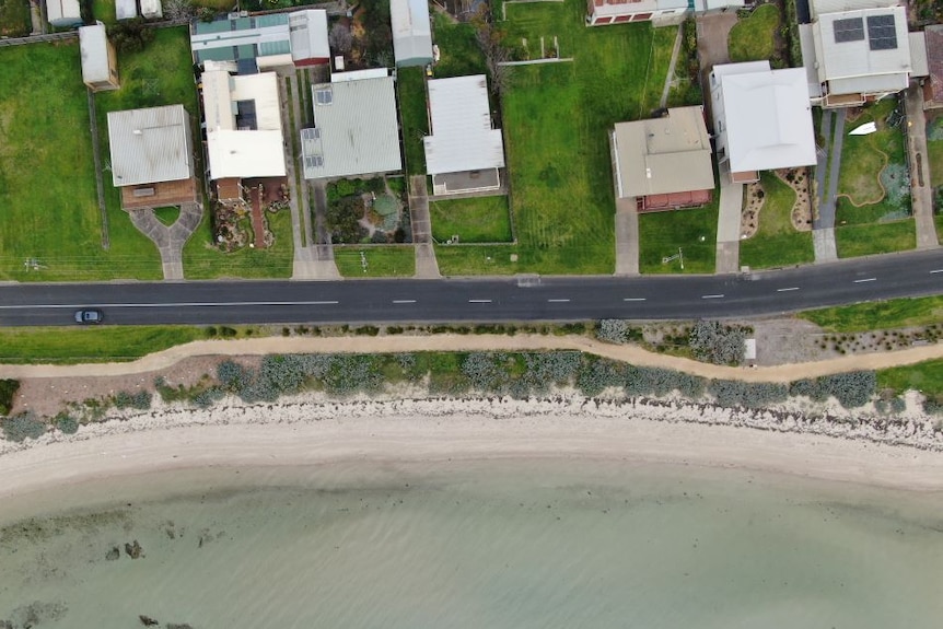 A drone photo shows homes located right beside the bay, separated only by a road and thin strip of dunes.