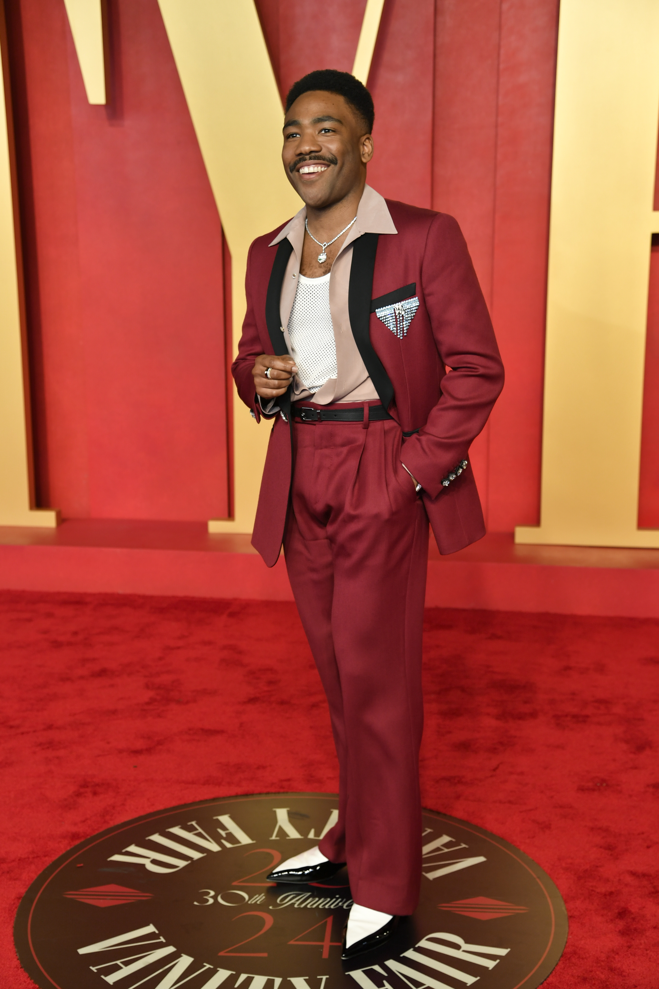 Donald Glover wearing a red suit with a dangly, sparkly brooch above the pocket 