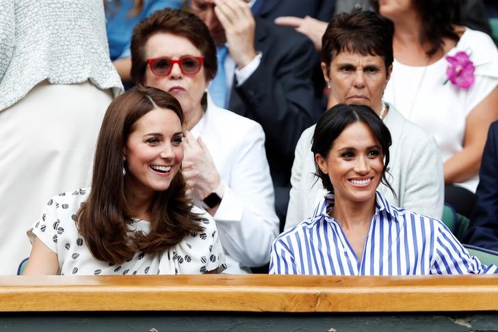 Kate sits to Meghan's left in white patterned dress, with Meghan wearing a blue and white striped shirt. Both are smiling.