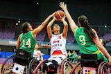 Three woman play wheelchair basketball together.