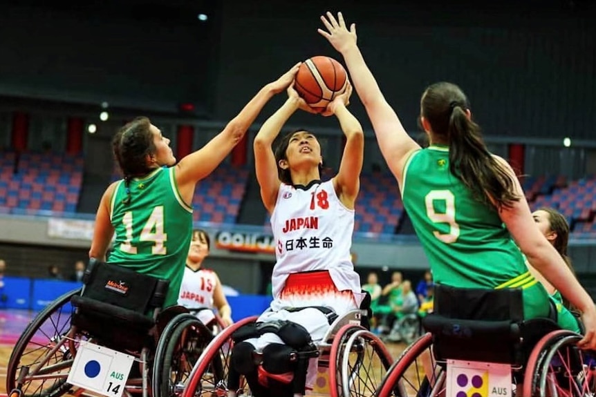 Three woman play wheelchair basketball together.