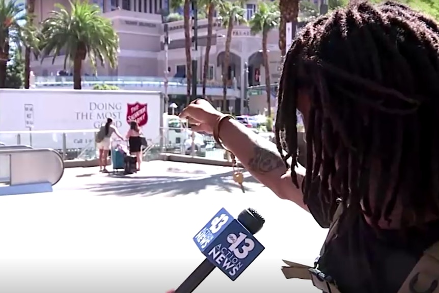 一名年轻的黑人男子在拉斯维加斯大道上与媒体交谈时举着长发绺的标语。