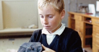 An old photograph of young boy holding a chunk of black rock.
