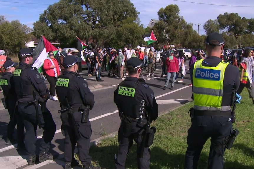 Police stand in a line in front of a group of protesters waving flags.