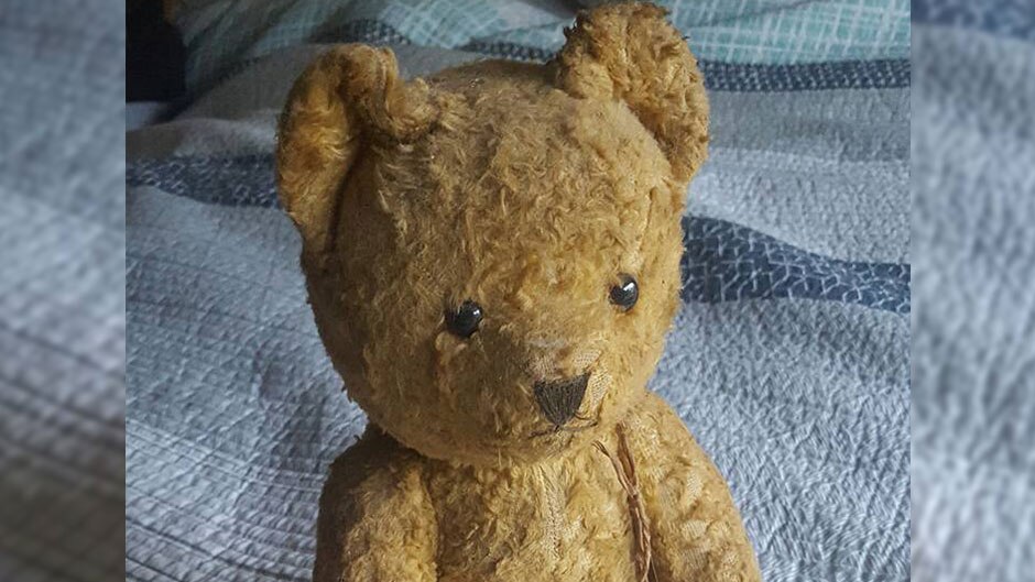 An old teddy bear sits on a quilt