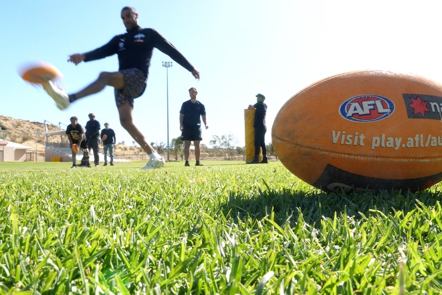 A football sits on the grass as somebody kicks another ball behind it