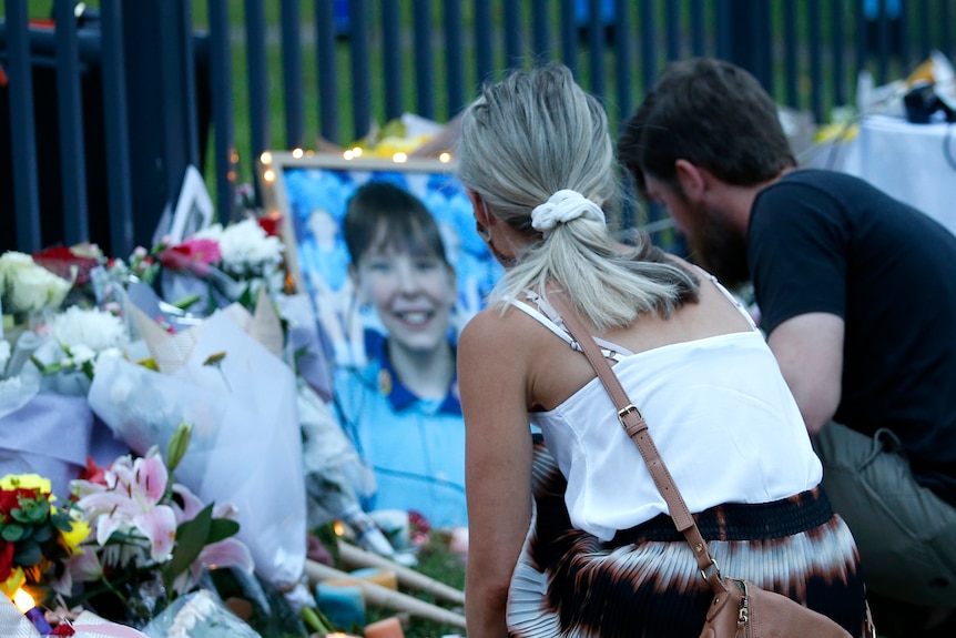 People placing flowers at a memorial for a deceased girl, her photo visible