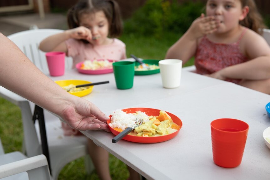 Kids eat at an outdoor table with a bowl of food in the foreground