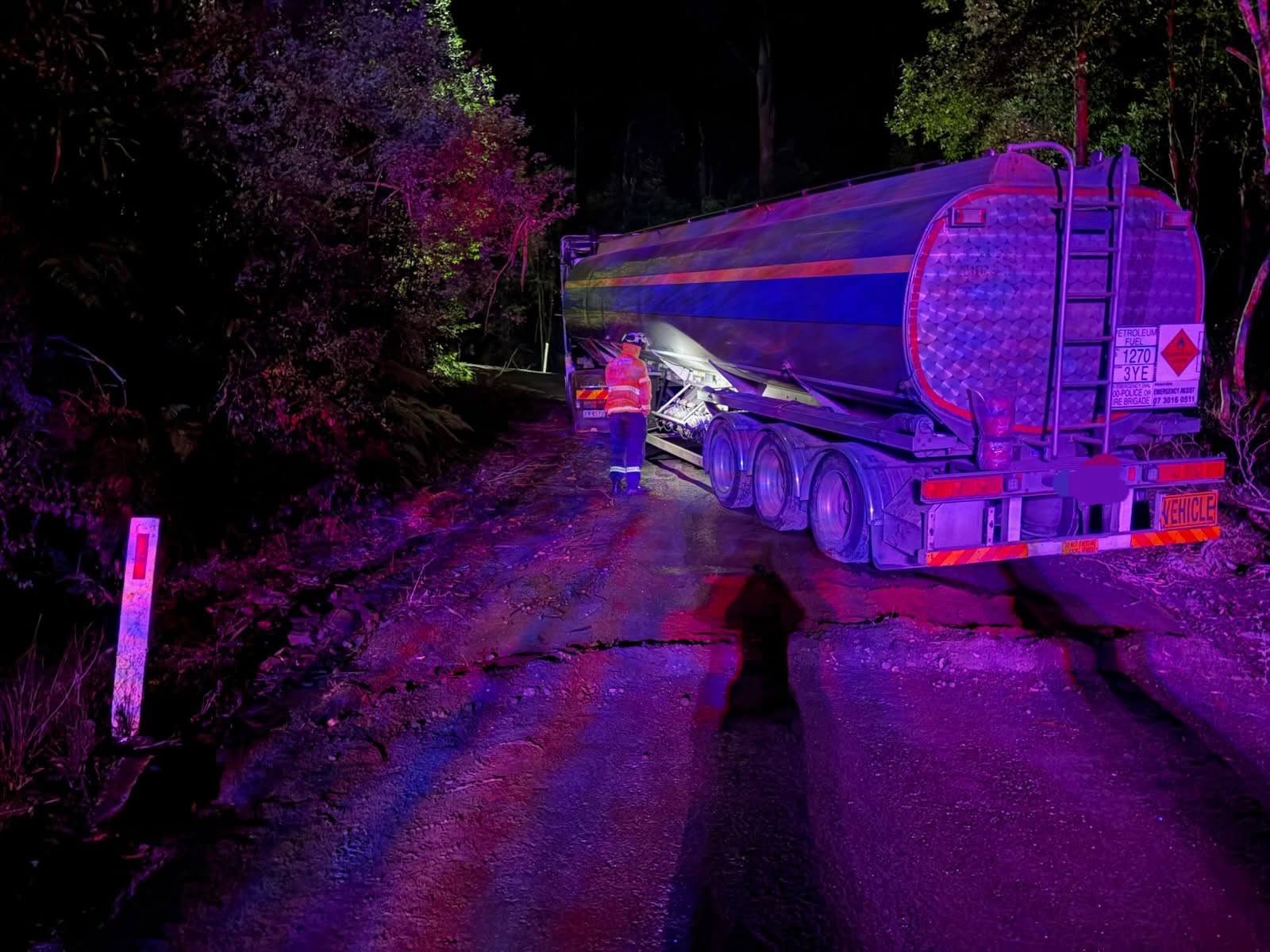 A tanker at night on a road with bush nearby.