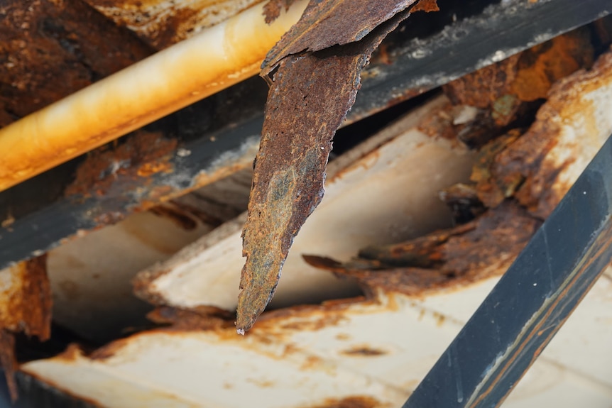 A damaged area on the underside of a metal roof, surrounded by rust.