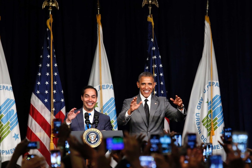 Barack Obama and Julian Castro stand on stage and wave to the crowd smiling