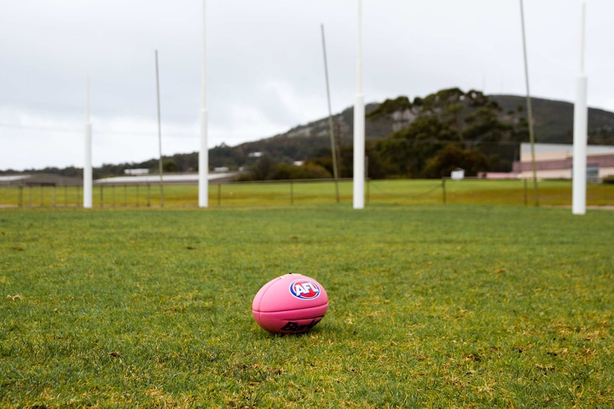 A pink AFL football on a grassed oval in front of the goal posts