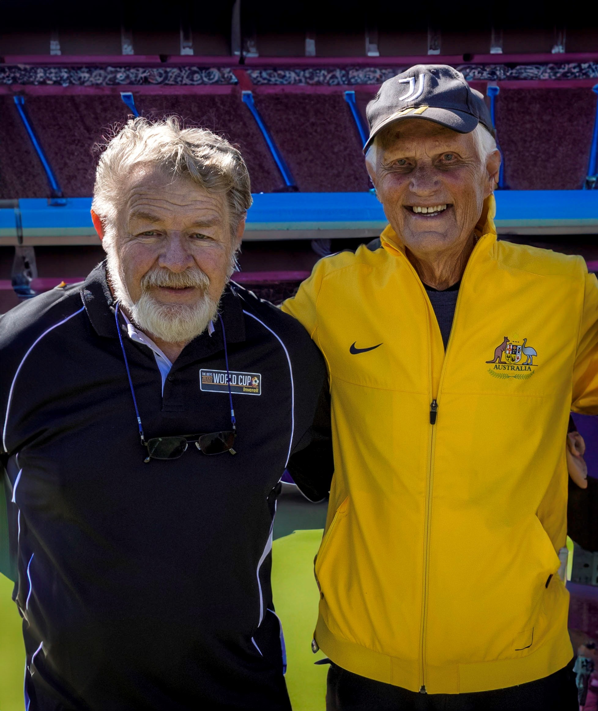 Two older gentleman are photographed looking into the camera in a stadium