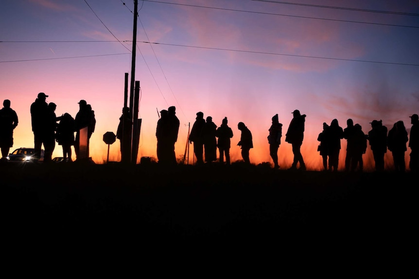 A group of people stand in a line as the sun sets in front of them