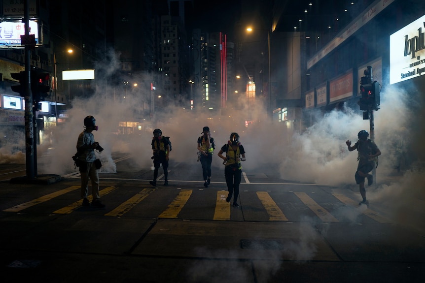 Emergency responders and journalists run from tear gas during a protest in Hong Kong.