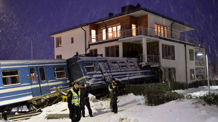 Policemen stand in front of train that derailed and crashed into a residential building in Sweden.