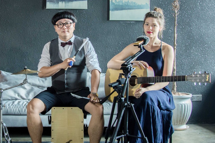 Chinese percussionist Chen Tong and Australian musician Emily Pritchard sit in a room next to each other holding instruments.