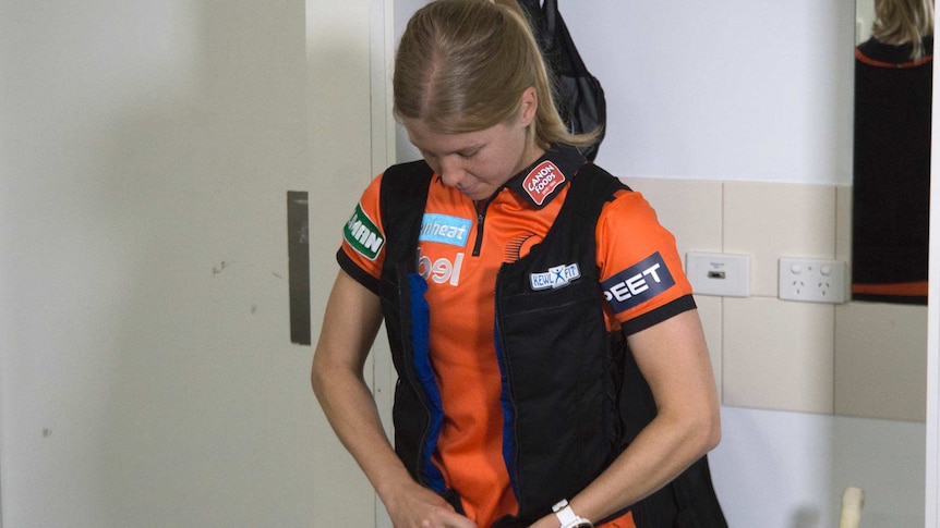 A mid shot of cricketer Jemma Barsby standing in a change room putting an ice vest on.