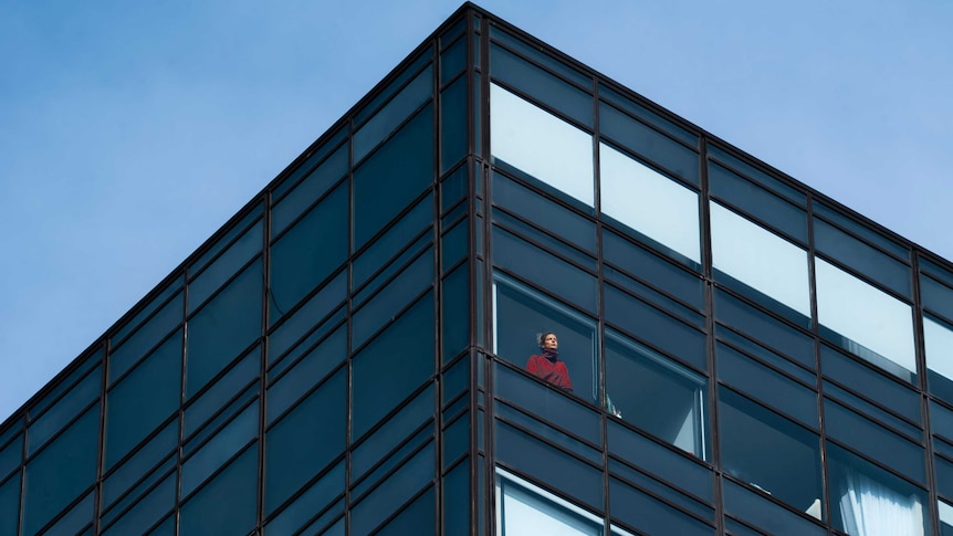 A young woman in a red jumper stares out the window of a high-rise hotel