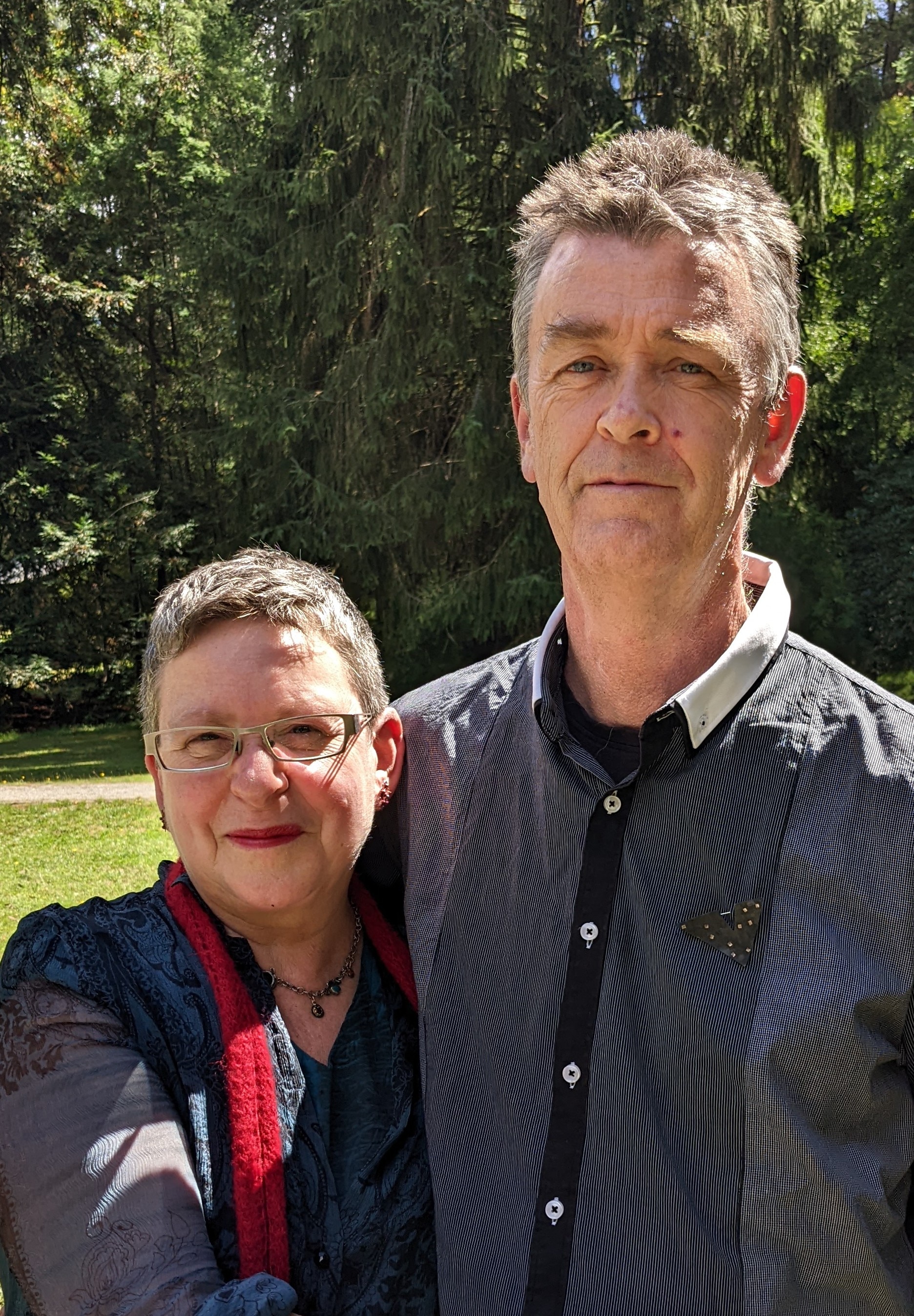 A mature aged couple hug side by side in a garden. 