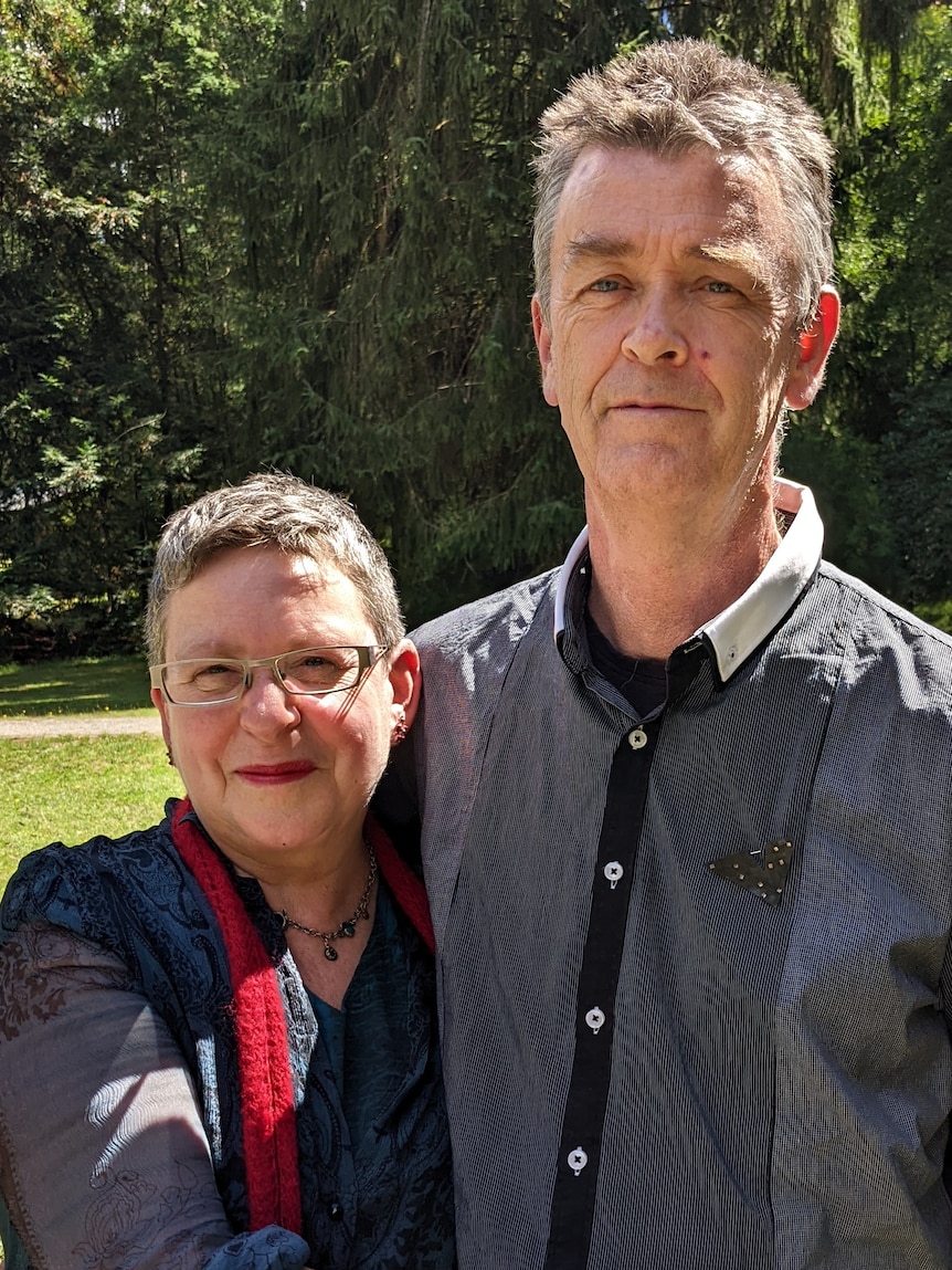 A mature aged couple hug side by side in a garden. 