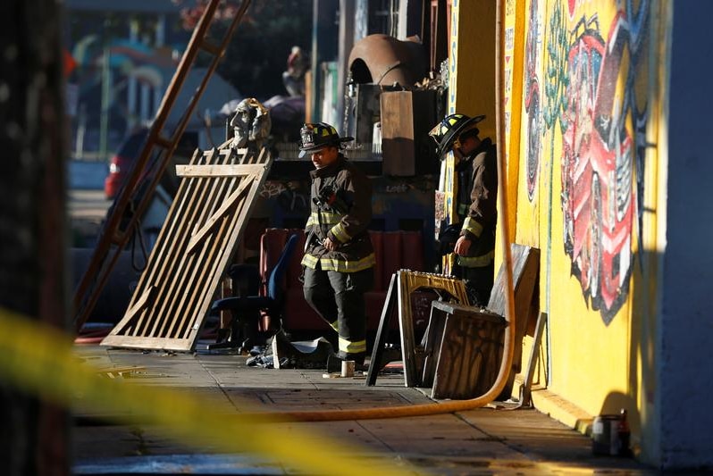 Firefighters exit a a warehouse with contents stacked at the doorway