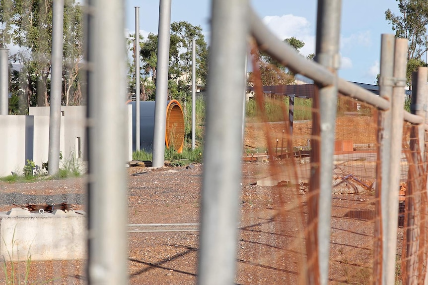 A view of abandoned playground equipment through a gap in a construction fence.