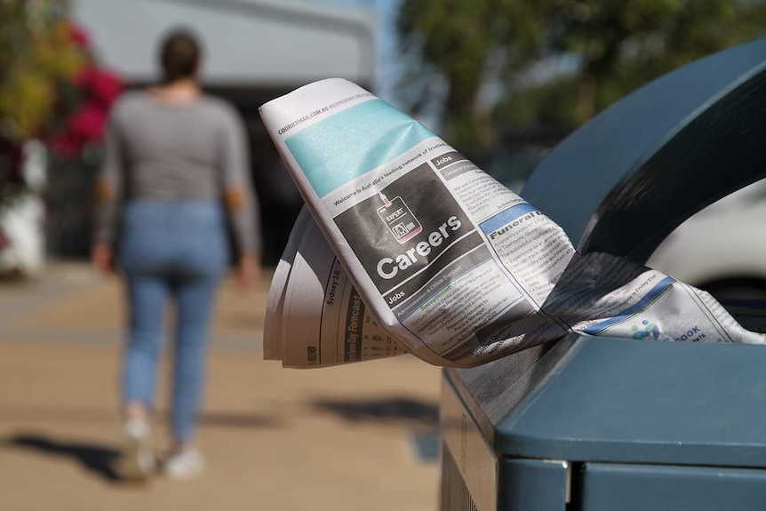 A woman walks away from newspaper jobs in a rubbish bin