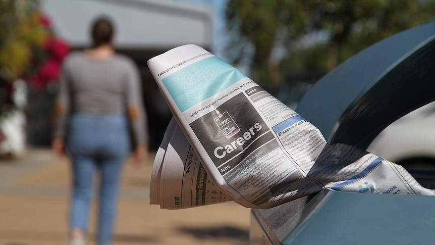 A woman walks away from newspaper jobs in a rubbish bin