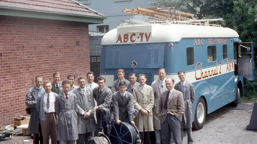 A group of men stand in front of a blue van marked "ABC-TV".