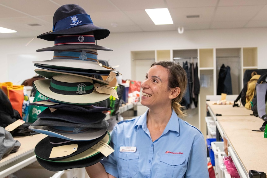 A woman holding a stack of lost school hats beside her.