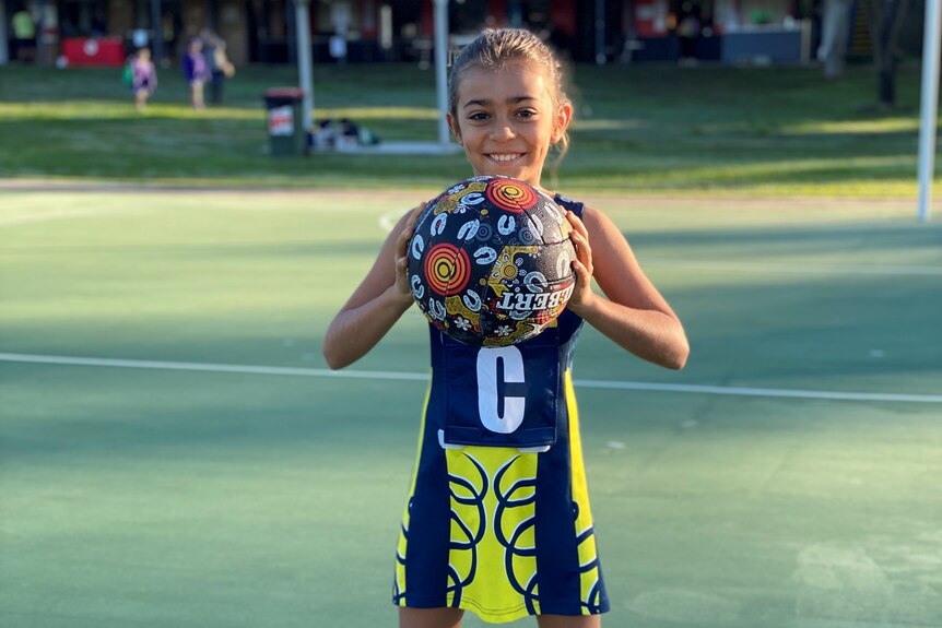 A Western Districts netballer holds a netball painted with Indigenous art.