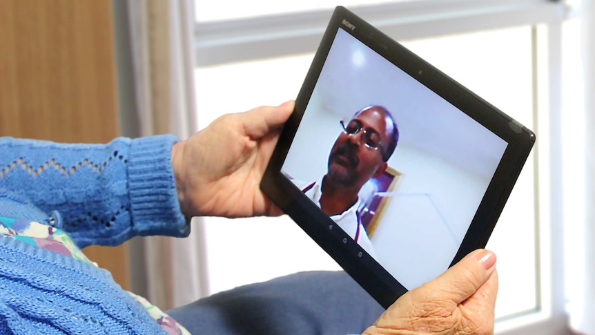An old lady holds an electronic tablet in two hands to communicate with a doctor on the screen