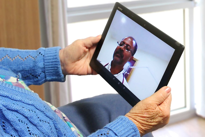 An old lady holds an electronic tablet in two hands to communicate with a doctor on the screen