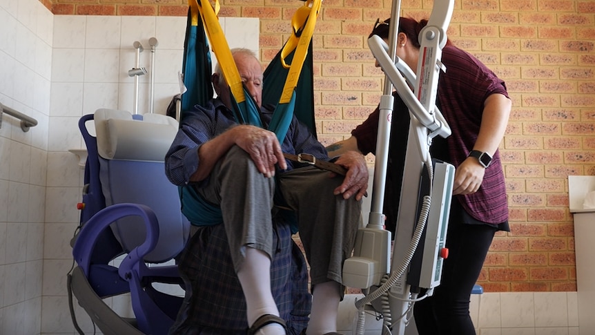 An elderly gentleman in a hoist being assisted by a carer in the bathroom