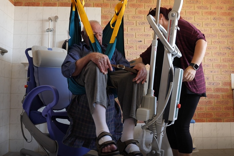 An elderly gentleman in a hoist being assisted by a carer in the bathroom