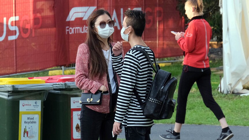 A man and woman wearing surgical masks stand outside at the Australian F1 Grand Prix.