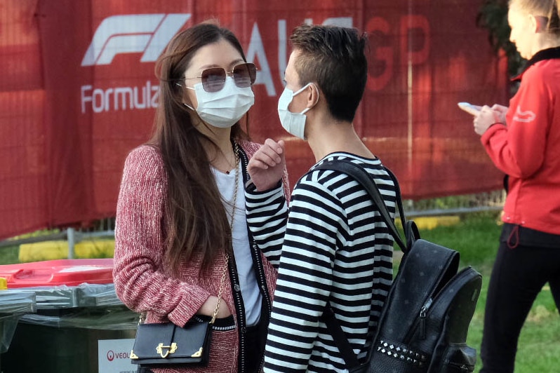 A man and woman wearing surgical masks stand outside at the Australian F1 Grand Prix.