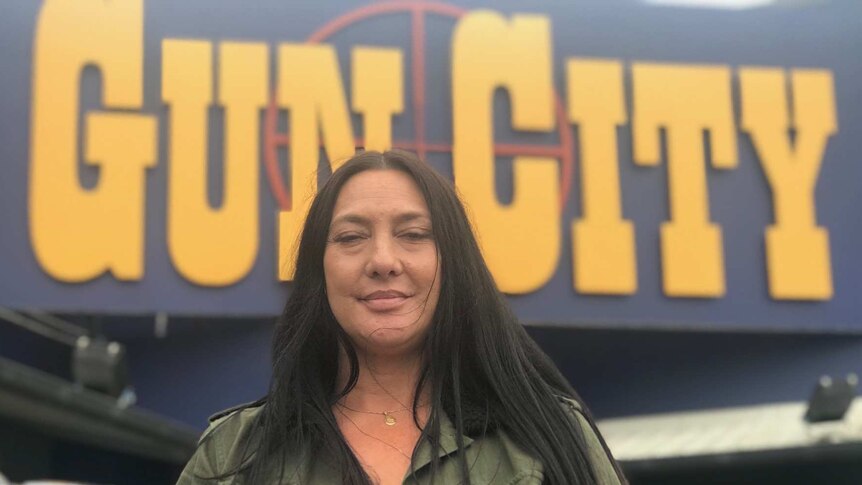 Carol Pomana wears a green jacket and stands in front of the 'Gun City' store in New Zealand