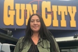 Carol Pomana wears a green jacket and stands in front of the 'Gun City' store in New Zealand