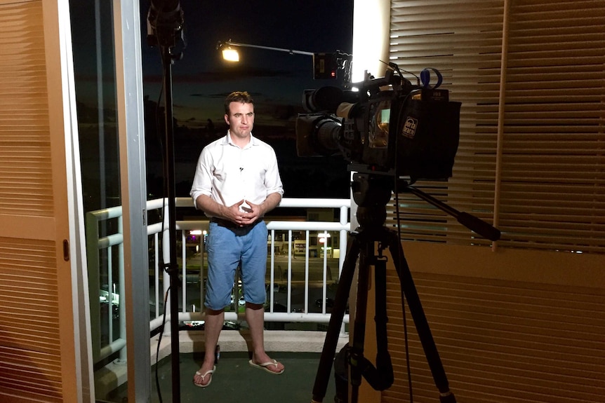 Journalist Andrew Greene standing on hotel balcony in Guam looking to camera on tripod for a live cross.