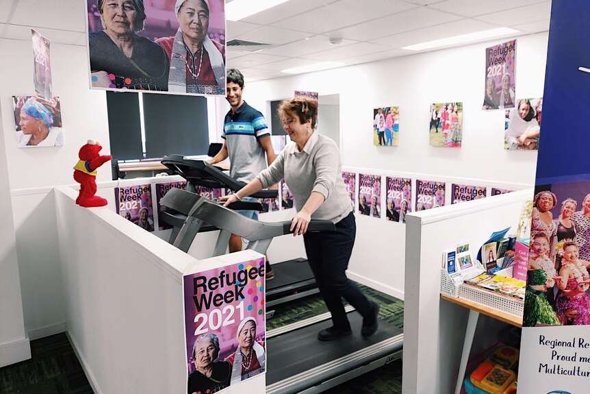 A woman and man walking on a treadmill in an office draped with colourful banners