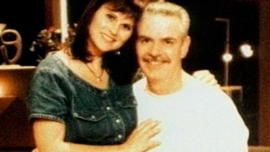 A man with a white t-shirt hugs a woman in a denim dress in an archive family photo.