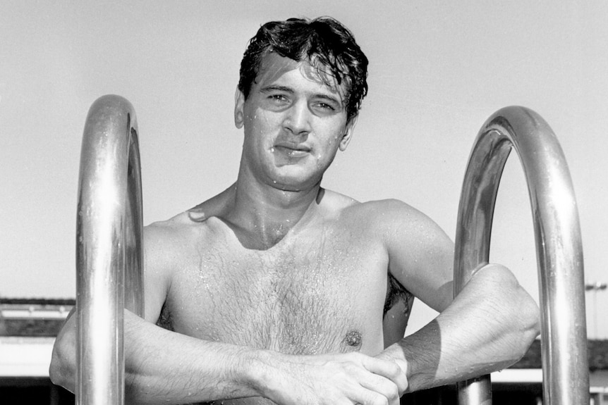 black and white image of American star Rock Hudson coming out of a swimming pool, wearing black trunks.