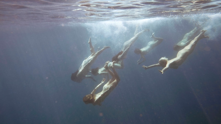 People dive into the ocean naked, as seen from under water.