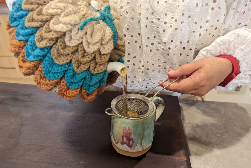 Ms Heward's hands pouring tea from a white pot with a tea cosy.