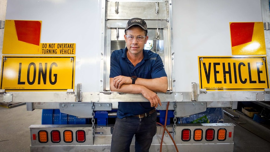 A man leans against the back of a semi-trailer.