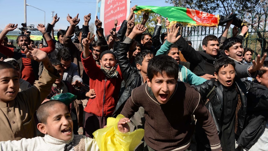 Young Afghan cricket fans celebrate by waving the Afghan flag in a street